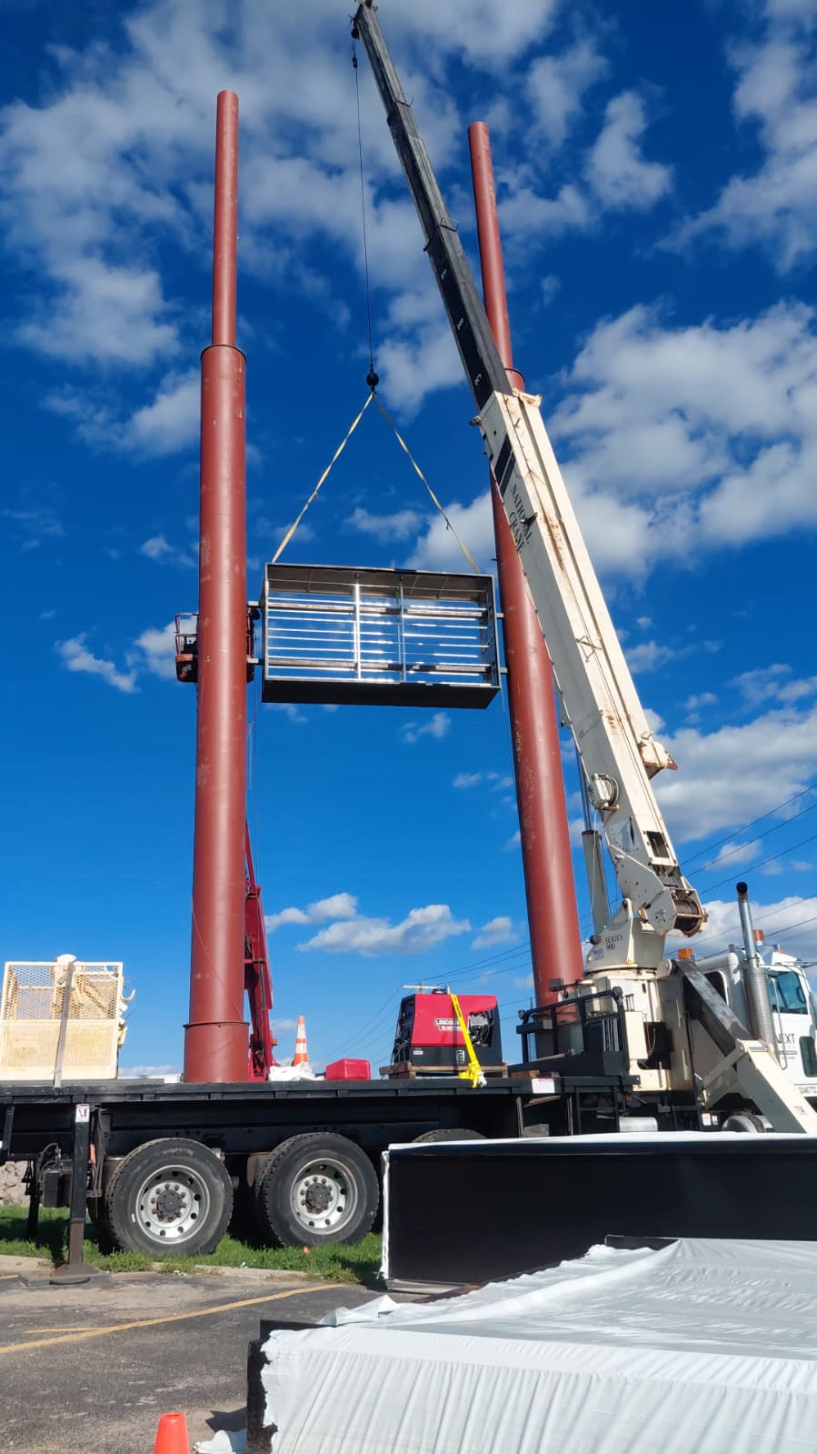 Crane lifting a large high-rise sign cabinet into position between steel support poles